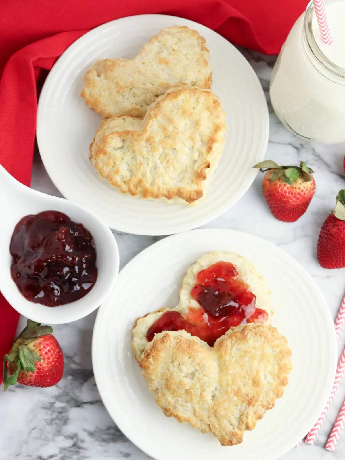 homemade heart shaped biscuits on plates with jam and strawberries.