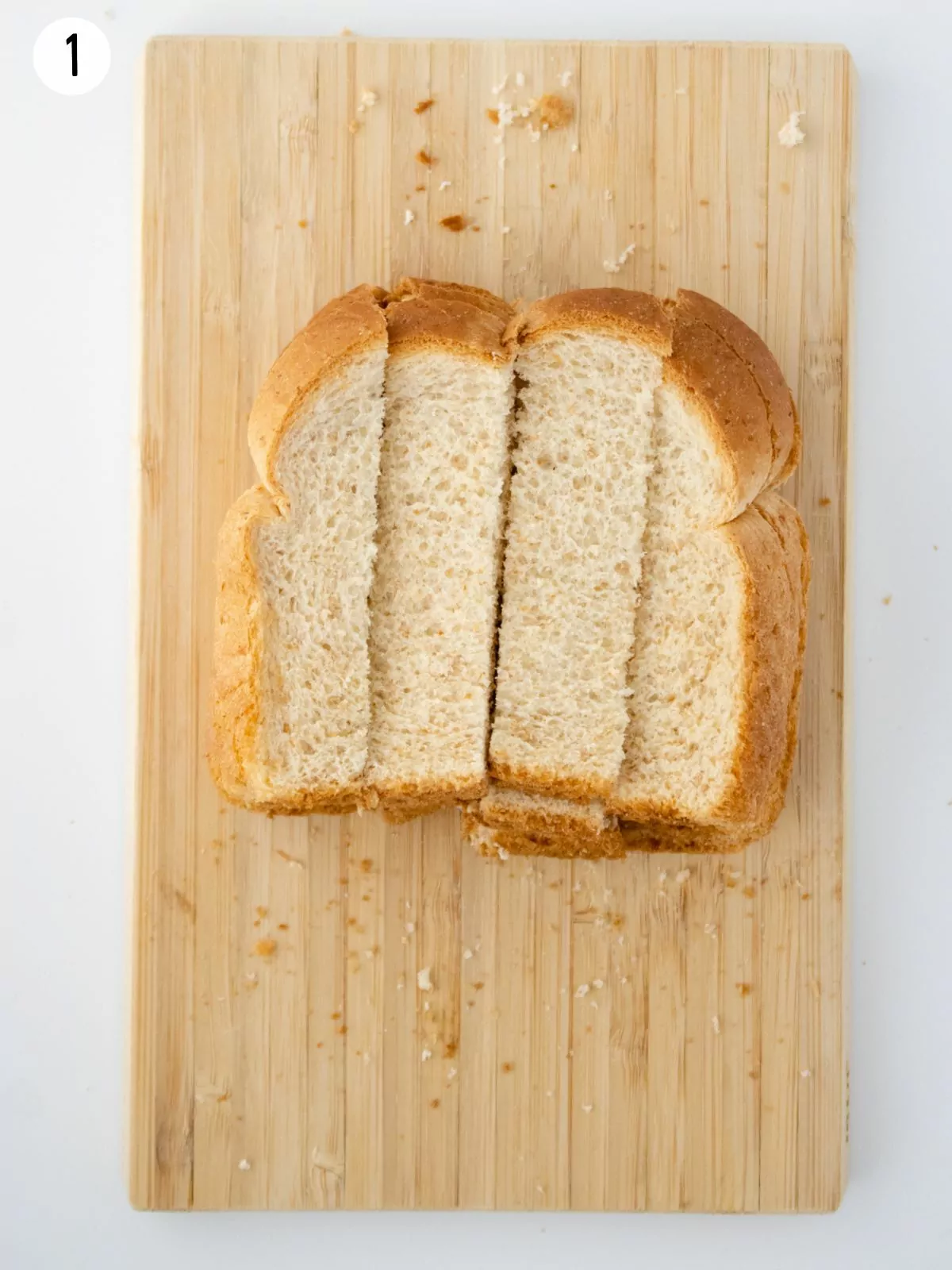 Sandwich bread sliced into 4 pieces on cutting board.