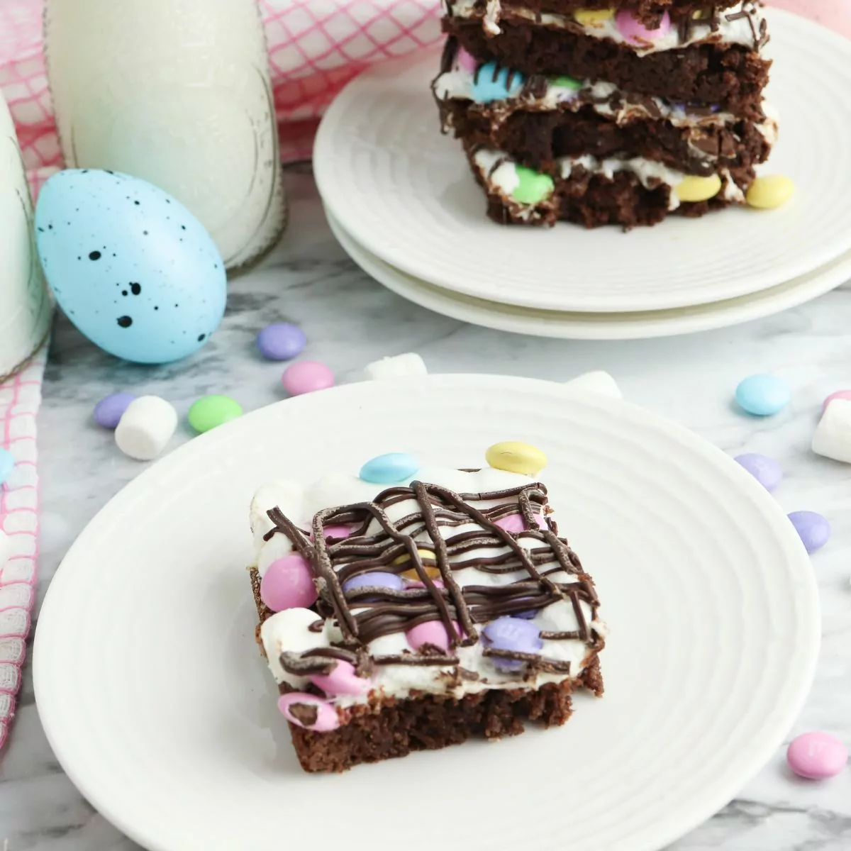 Brownie topped with melted marshmallows, M&Ms, and chocolate drizzle served on a white plate