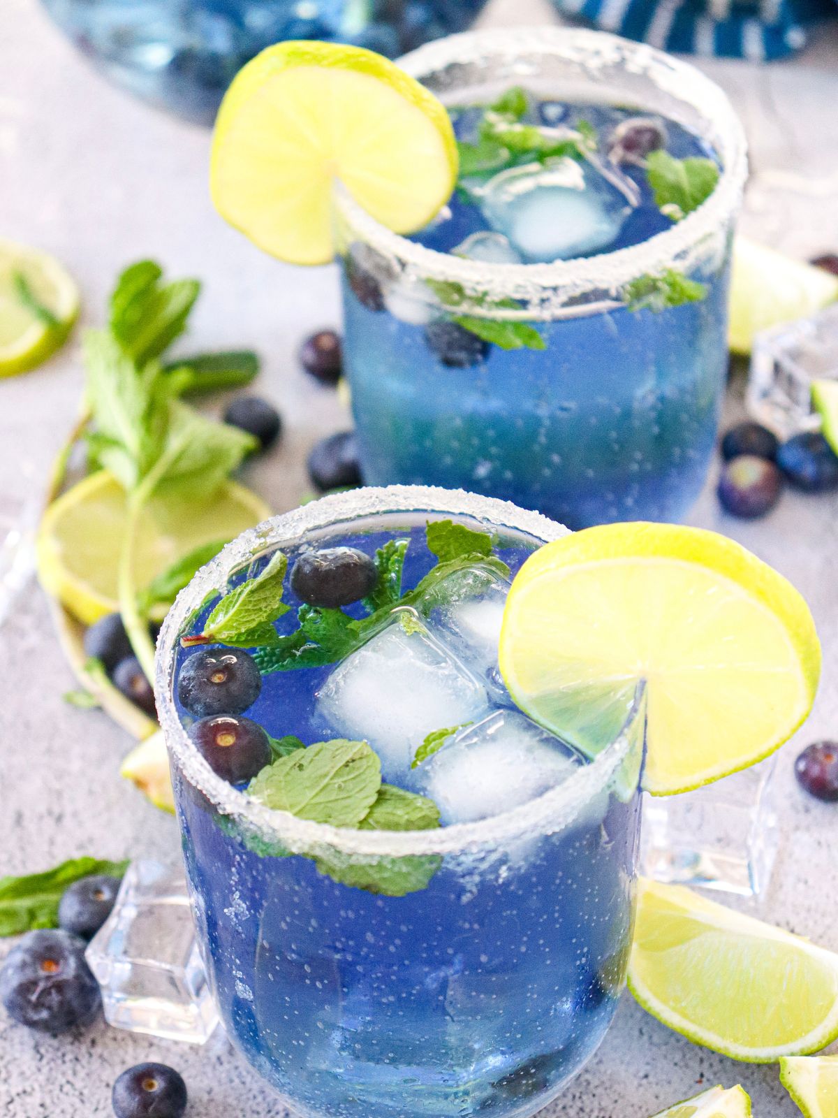 2 glasses of blueberry infused water with lime slices and mint leaves.