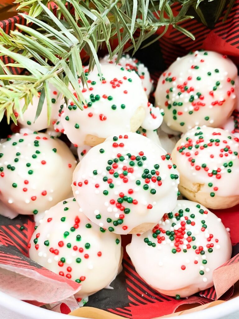 cookies with Christmas sprinkles on top of a buffalo check paper napkin and a sprig of pine.