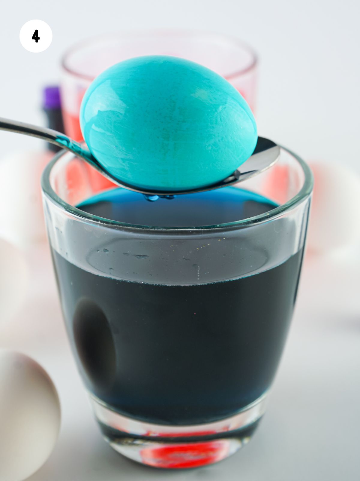 blue dyed egg on spoon being held over a glass of blue colored water.