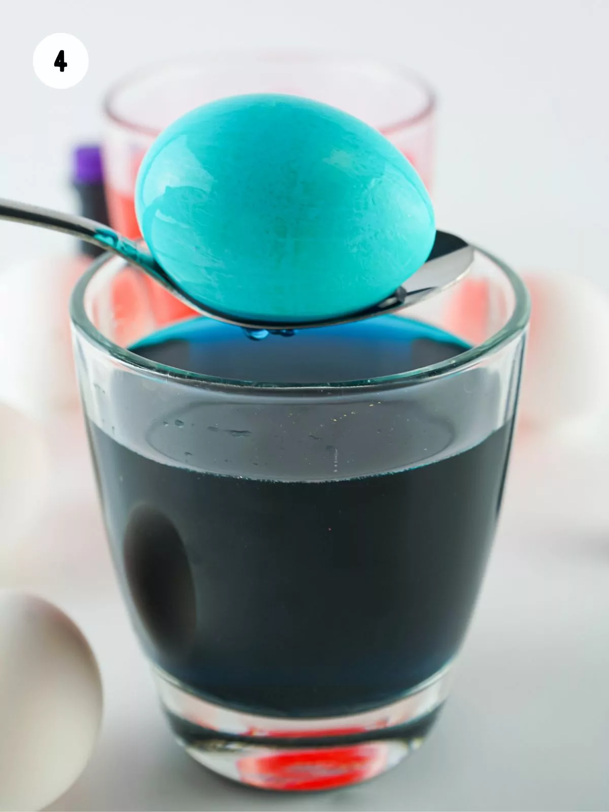 blue dyed egg on spoon being held over a glass of blue colored water.