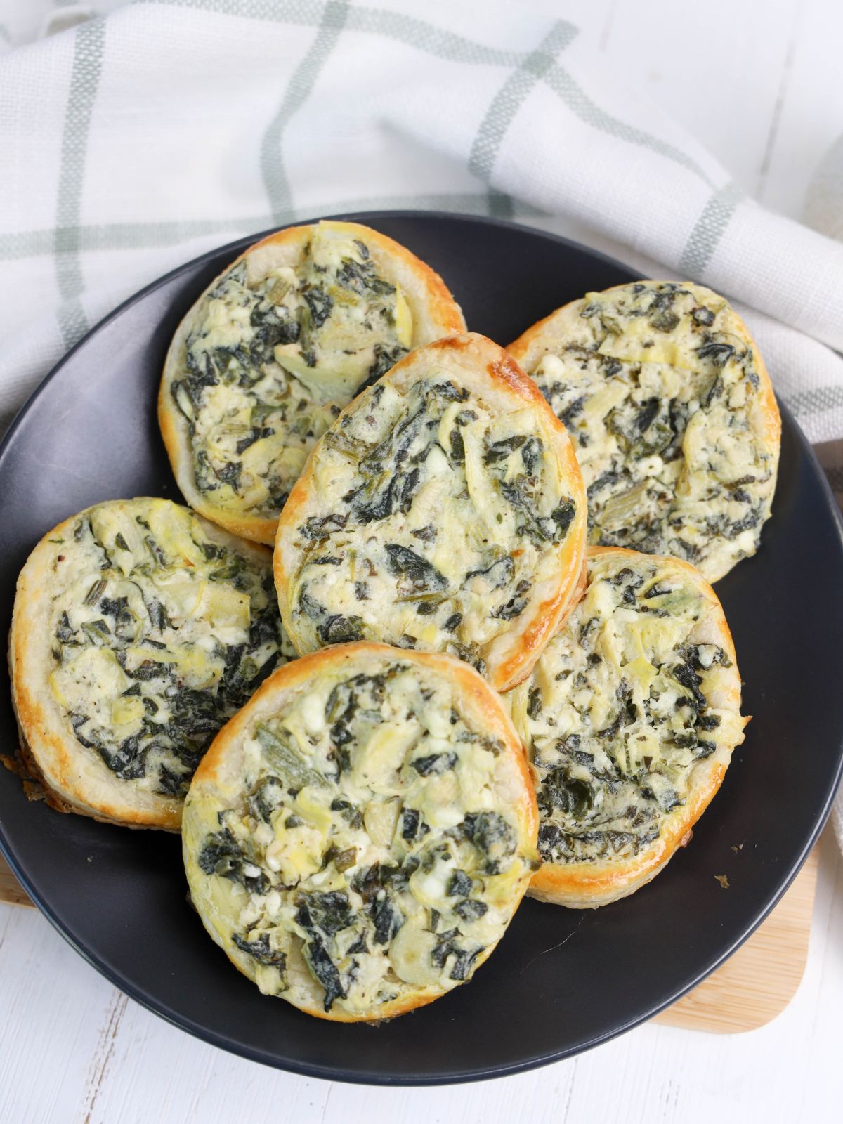 puff pastry eggs with spinach artichoke dip baked and on black plate.