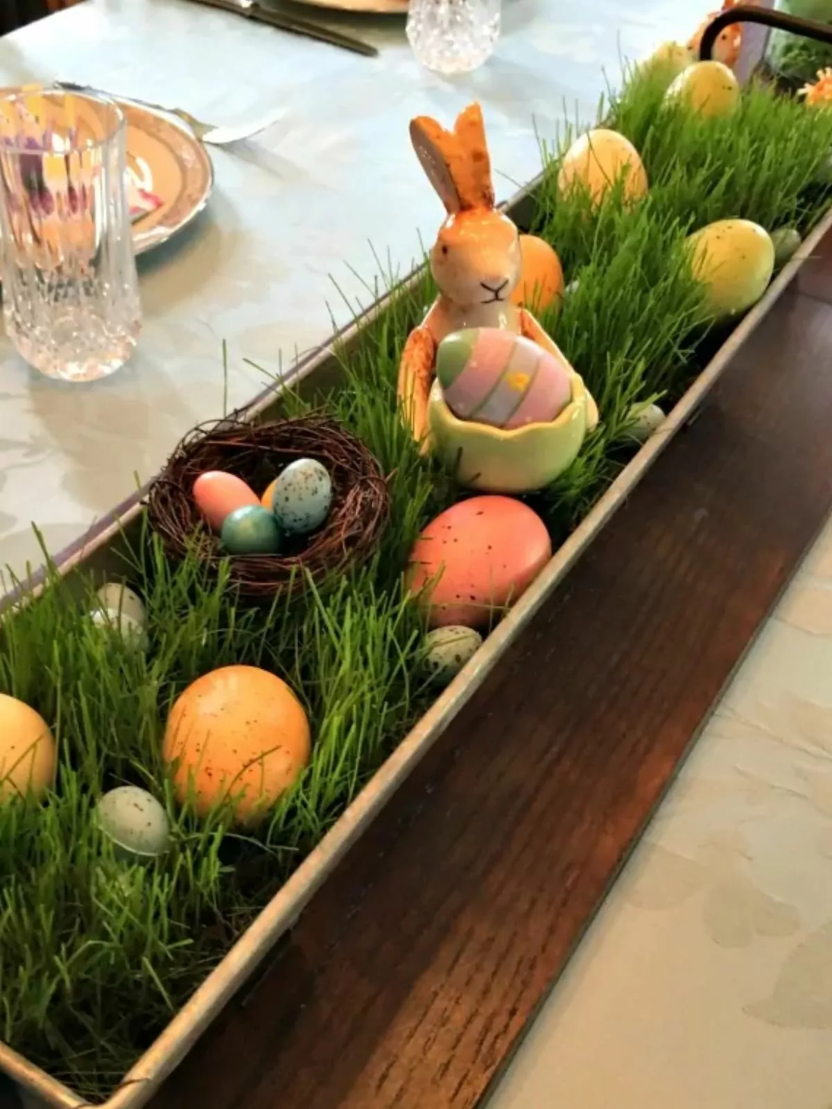 grass centerpiece decorated with fake eggs and a ceramic bunny.