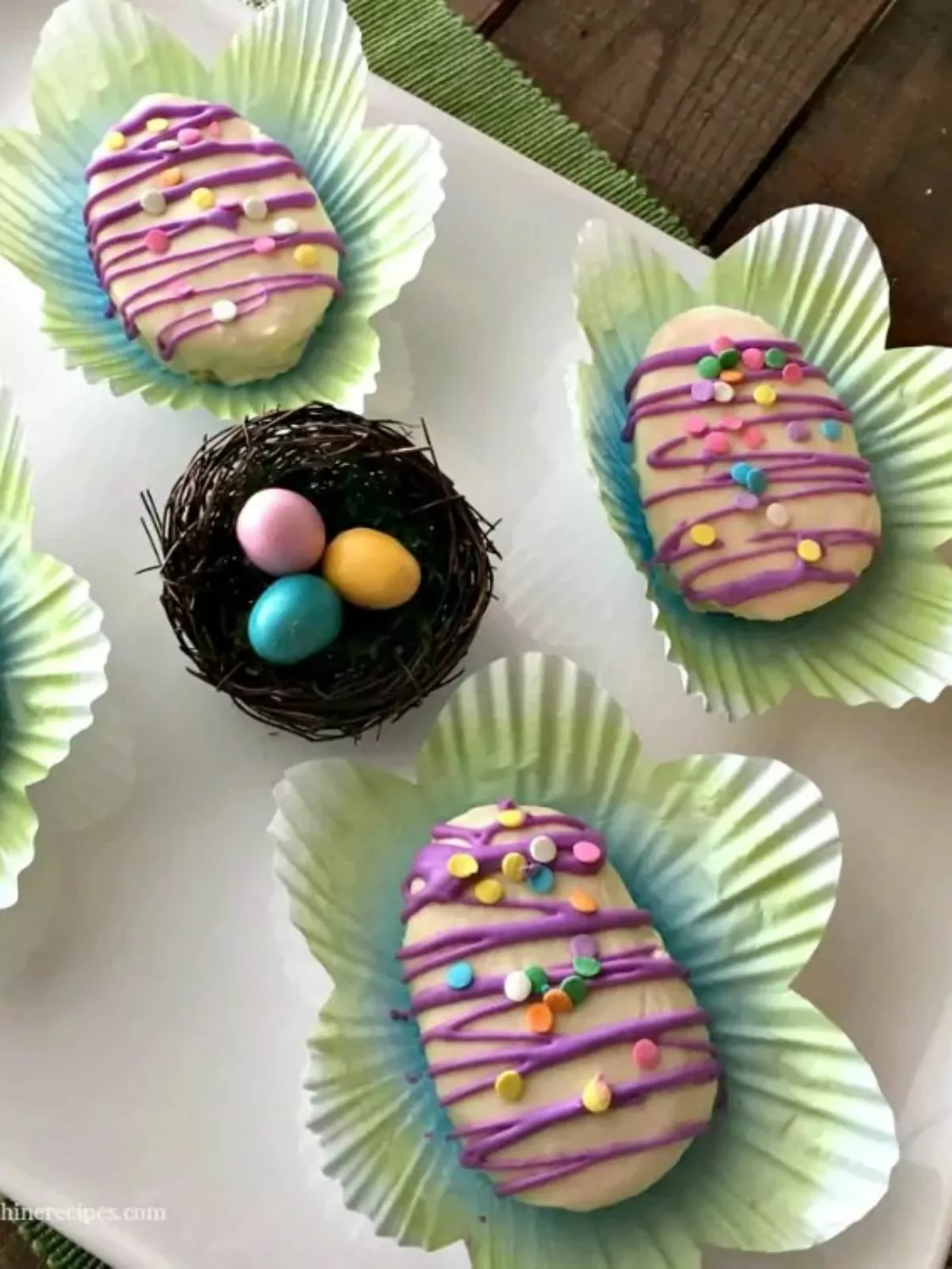 decorated cakes in the shape of eggs in cupcake liner on white plate.