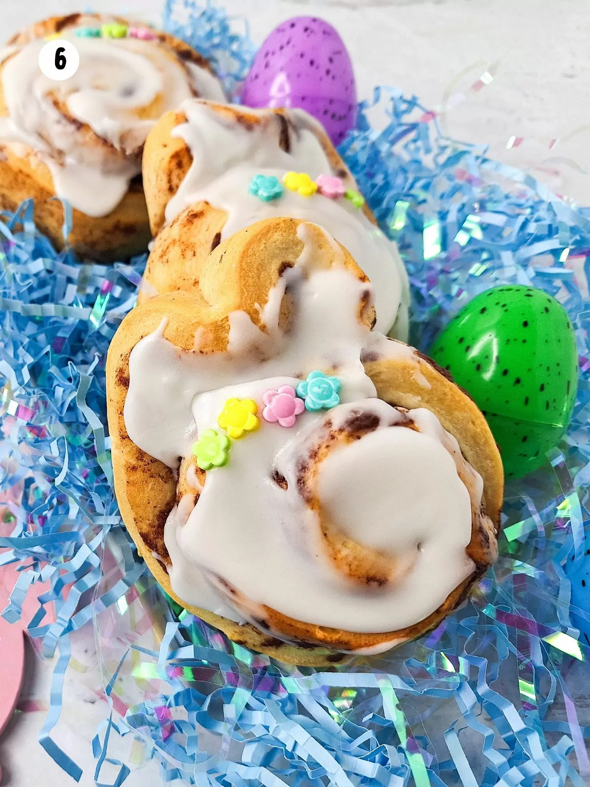 cinnamon rolls dressed up as bunnies on top of blue shredded paper.