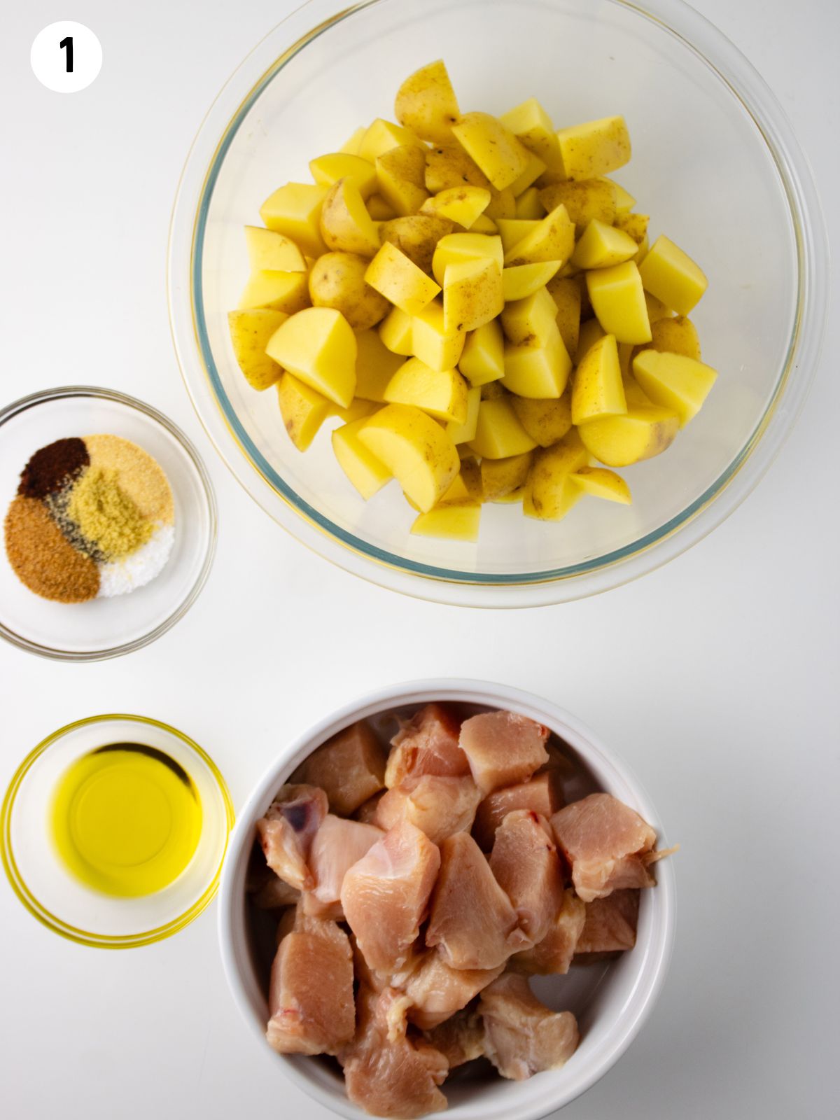 chicken in bowl, potatoes in bowl, bowls of seasoning and oil.