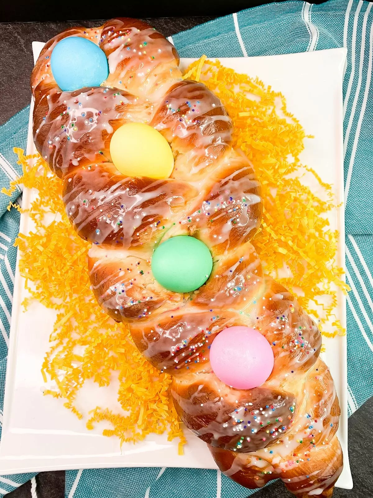 loaf of braided Easter bread with colored eggs on white tray.