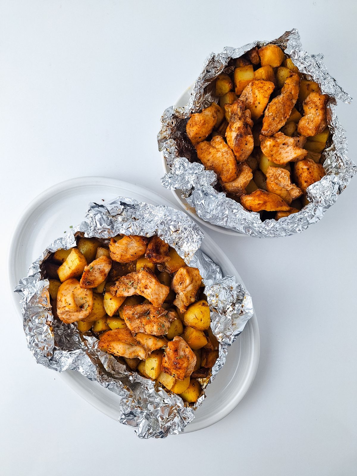 cooked chicken, potatoes bundles in aluminum foil on plate.