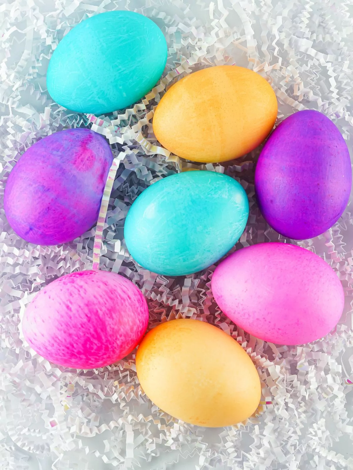 different colored eggs laying flat on white paper shred.