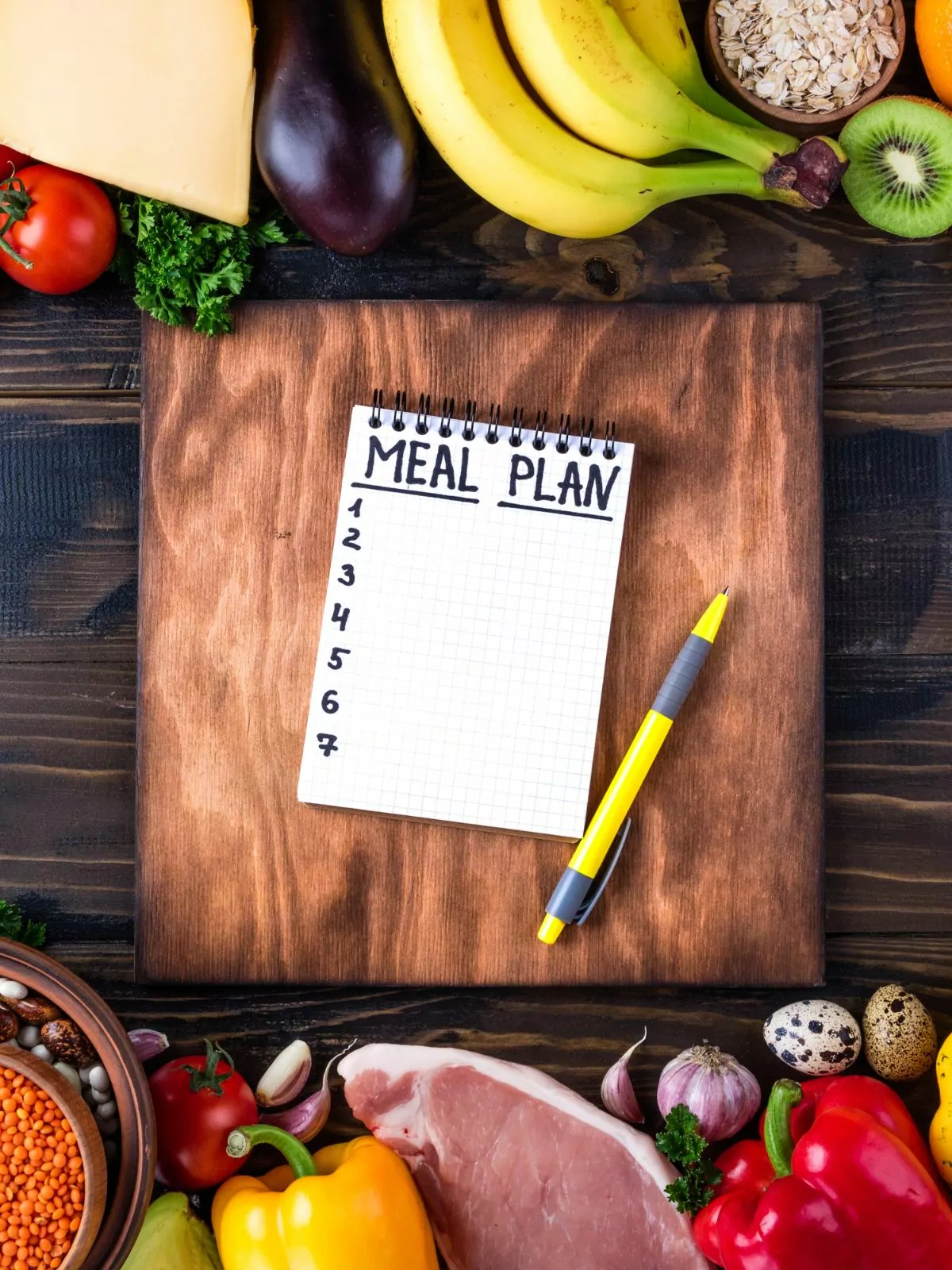 meal plan notebook on cutting board with fruits, vegetables and meat.