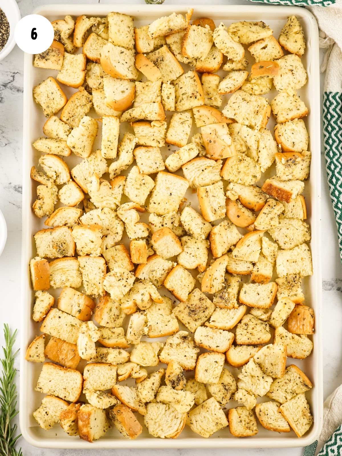 cubed bread with melted butter and herbs on baking tray.