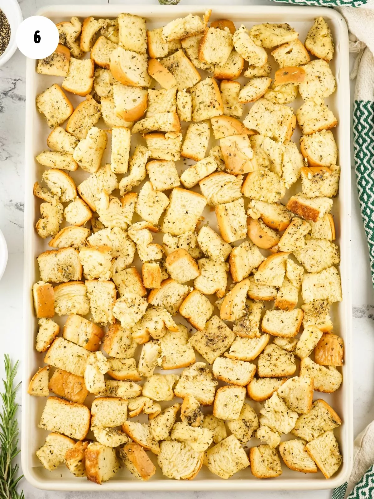 cubed bread with melted butter and herbs on baking tray.