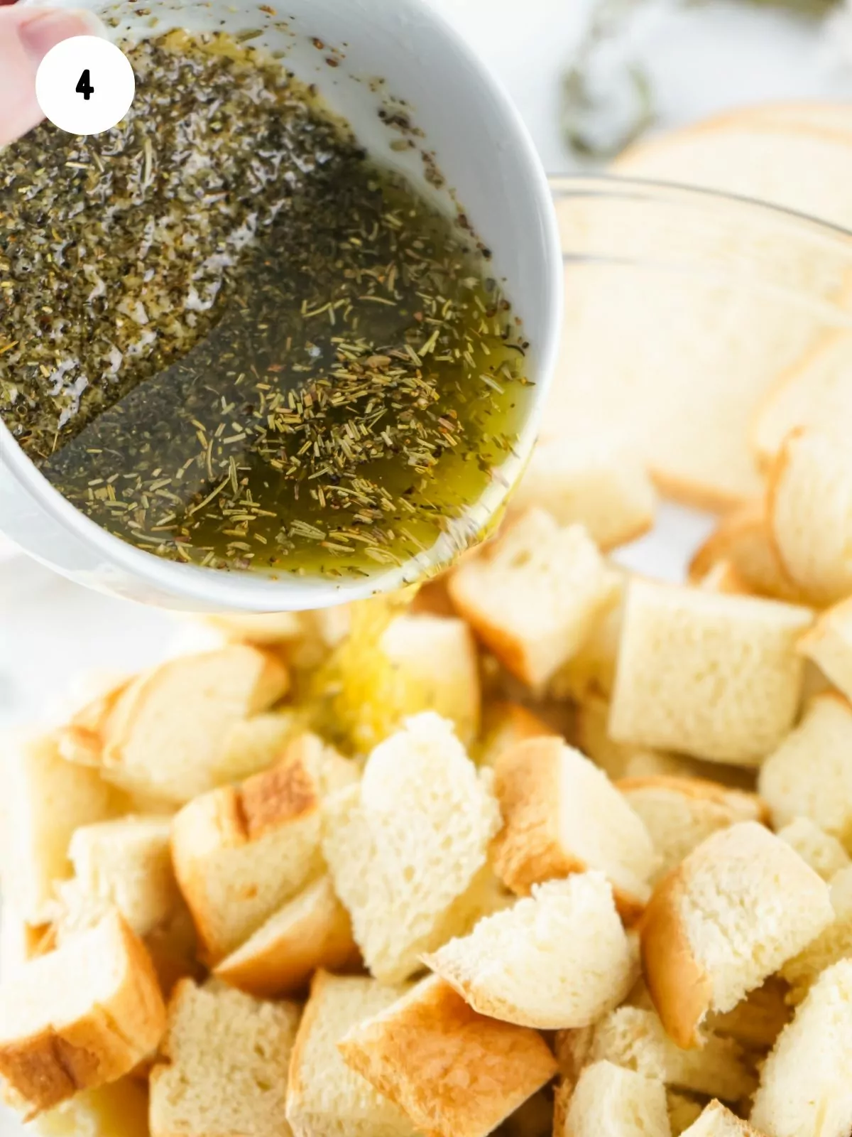 small bowl with melted butter and herbs being poured on top of cubed bread.