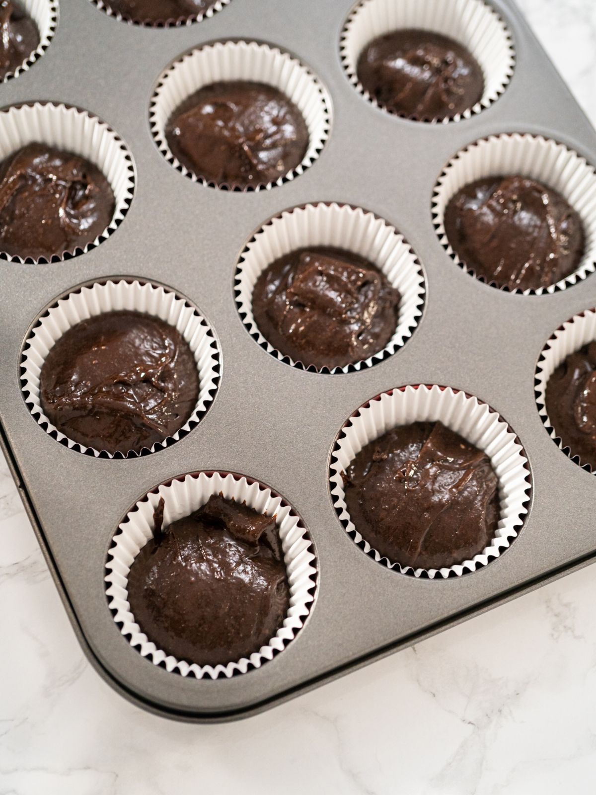 Muffin pan filled with unbaked chocolate muffin batter.
