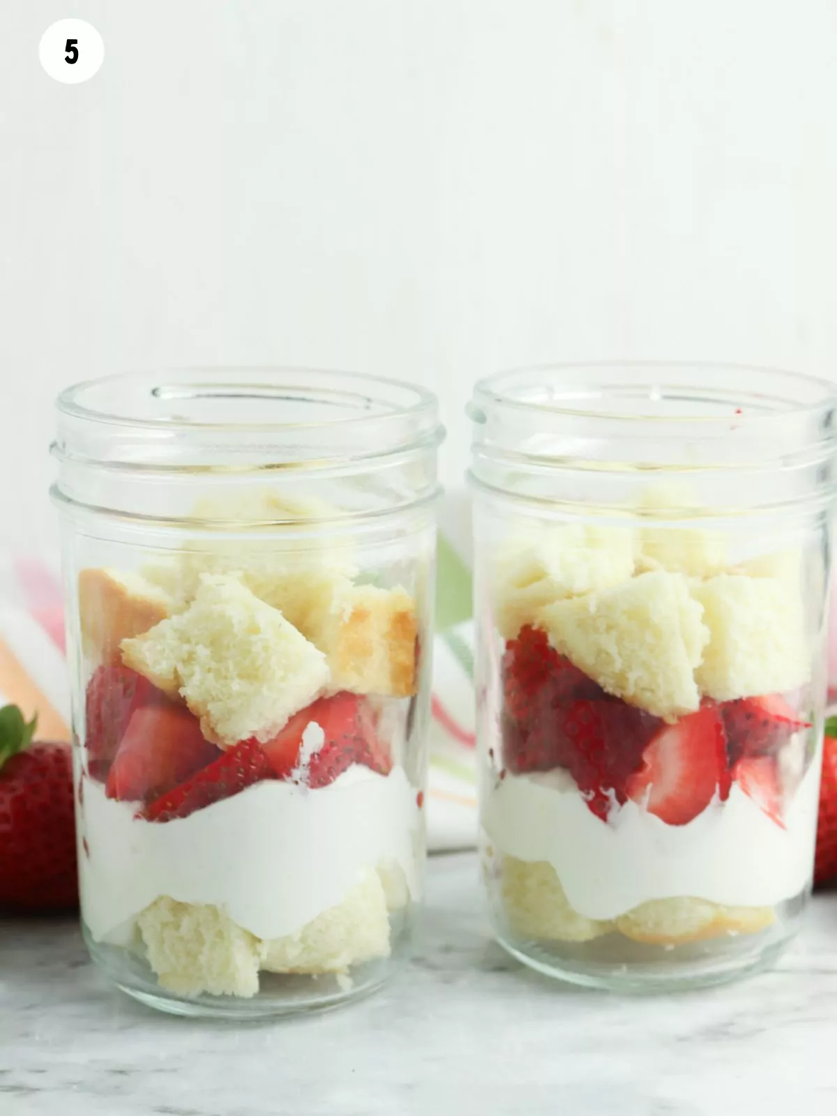 pieces of pound cake with strawberries and whipped cream in mason jars.