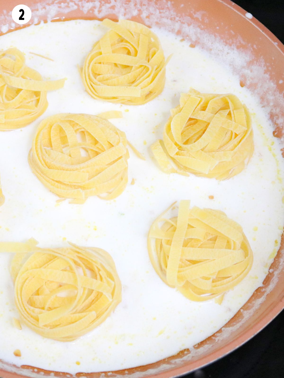 pasta noodle bundles in Alfredo sauce in pan.