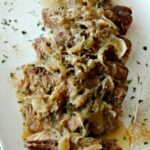 Sliced London broil with caramelized onions on a white plate.