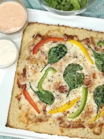 low carb pizza with peppers, spinach and cheese on white plate.