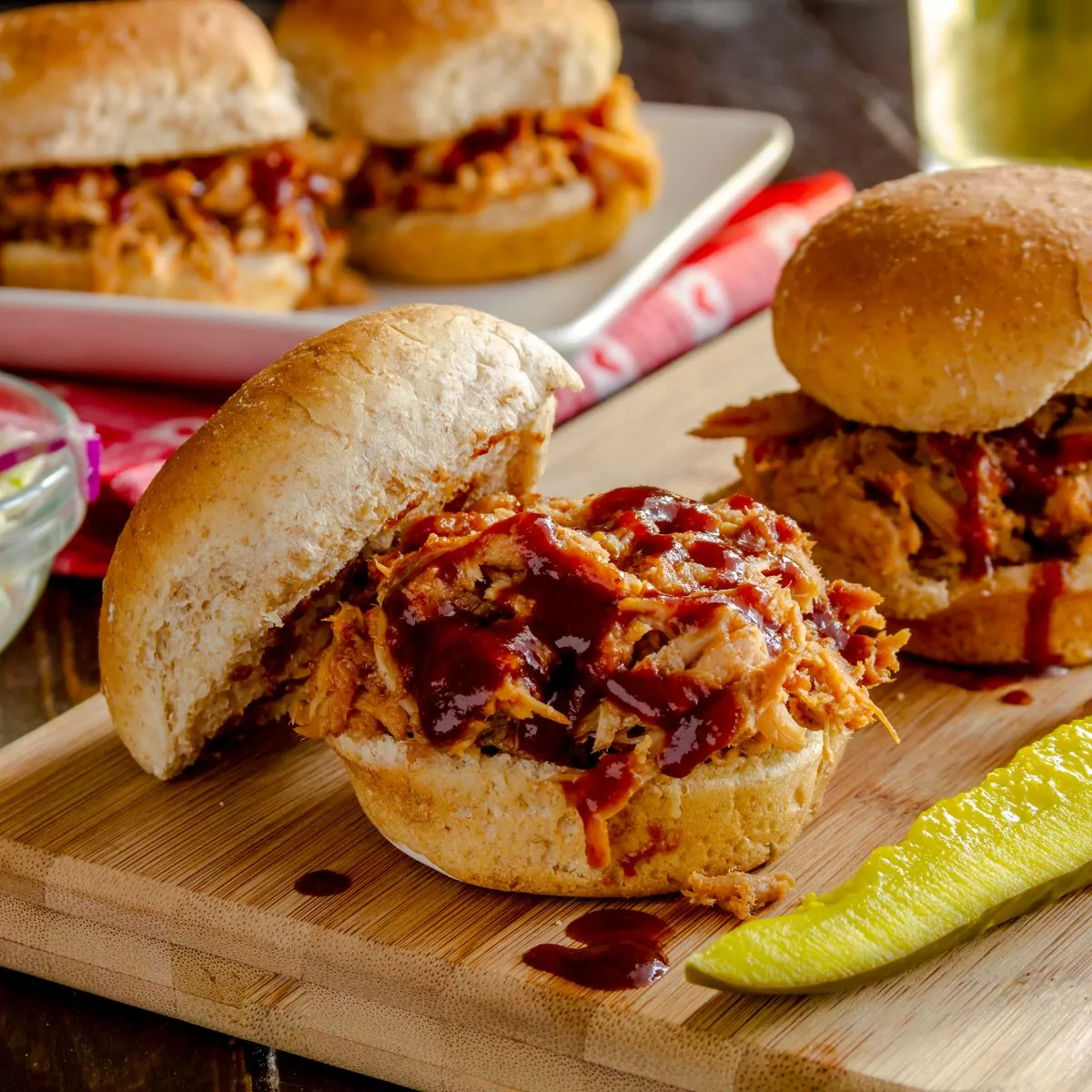pulled chicken sandwiches with pickle on cutting board.