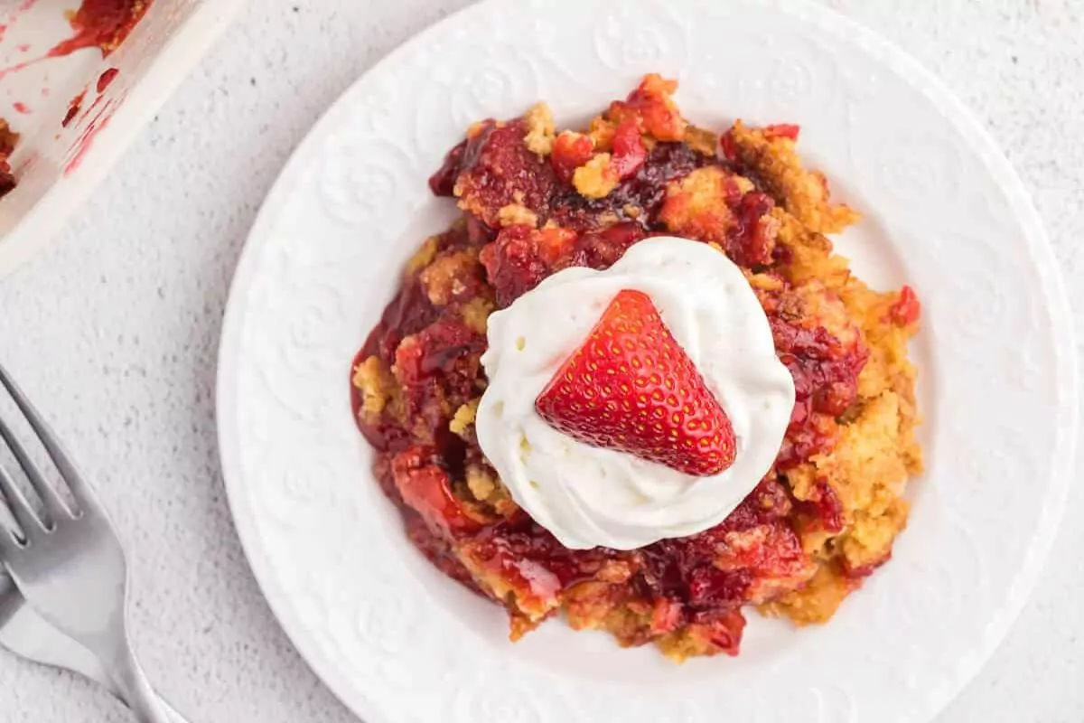 Strawberry Dump Cake topped with whipped cream and a fresh strawberry half.