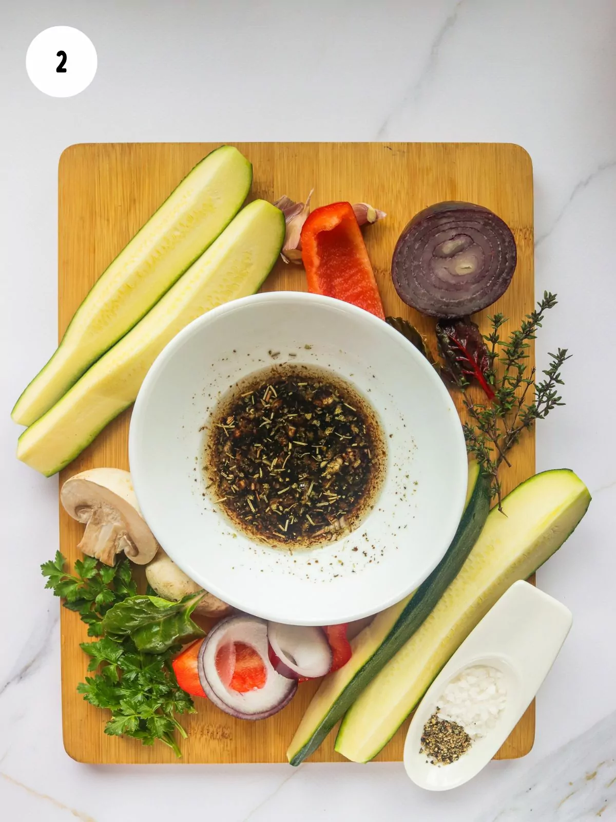 different vegetables on cutting board with bowl of oil and seasonings.