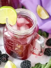 mason jar glass of blackberry mocktail with lime slices and fresh mint leaves.