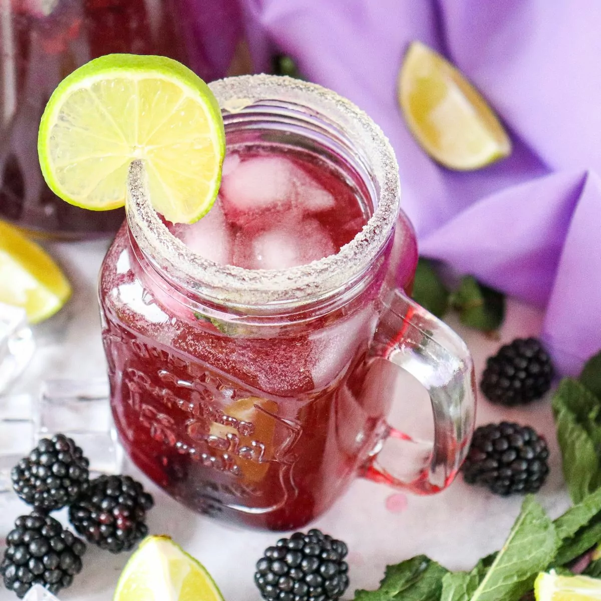 mason jar glass of blackberry mocktail with lime slices and fresh mint leaves.