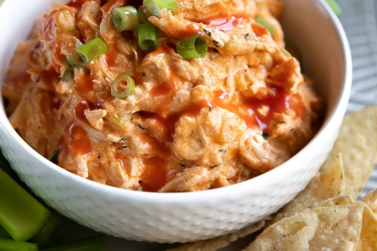a dip in a bowl with green onions on top.