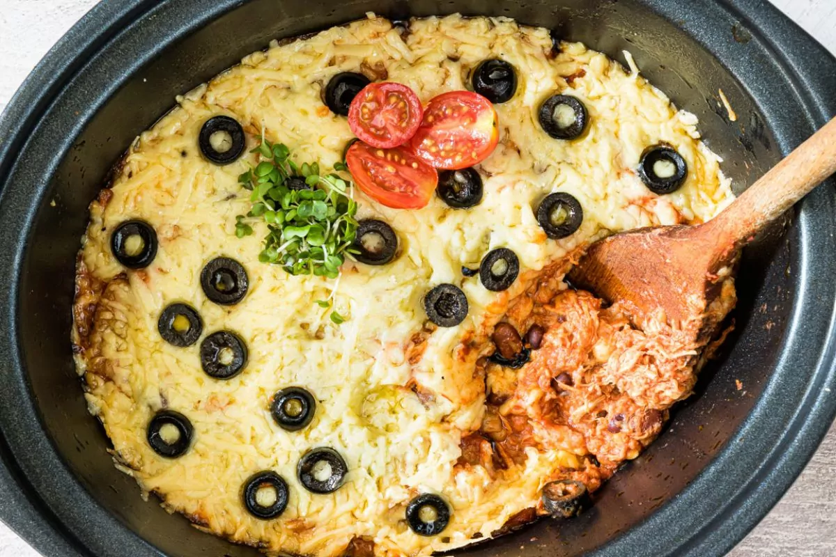 Enchilada chicken casserole made in a crock pot with wooden spoon. Topped with black olives.