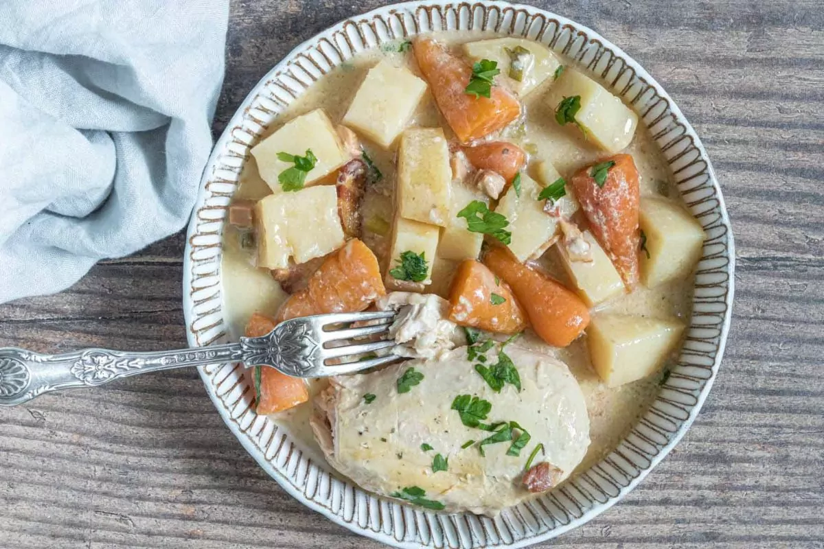 cooked chicken with cubed potatoes and carrots in a cream sauce in a plate with fork.