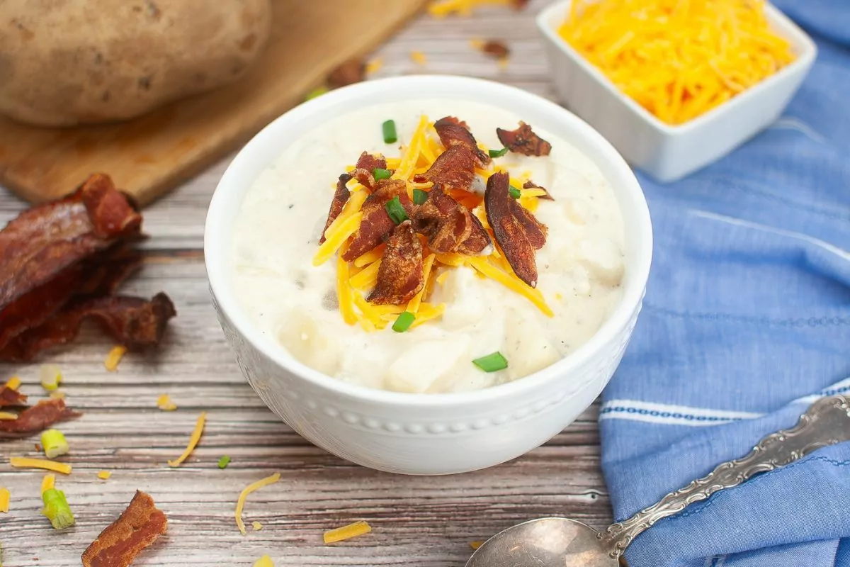 white bowl of potato soup topped with shredded cheese and bacon pieces.