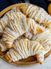 wooden plate filled with lemon crescent rolls and 2 lemons on the side.