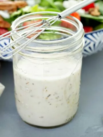 creamy salad dressing in mason jar with wire whisk on top.