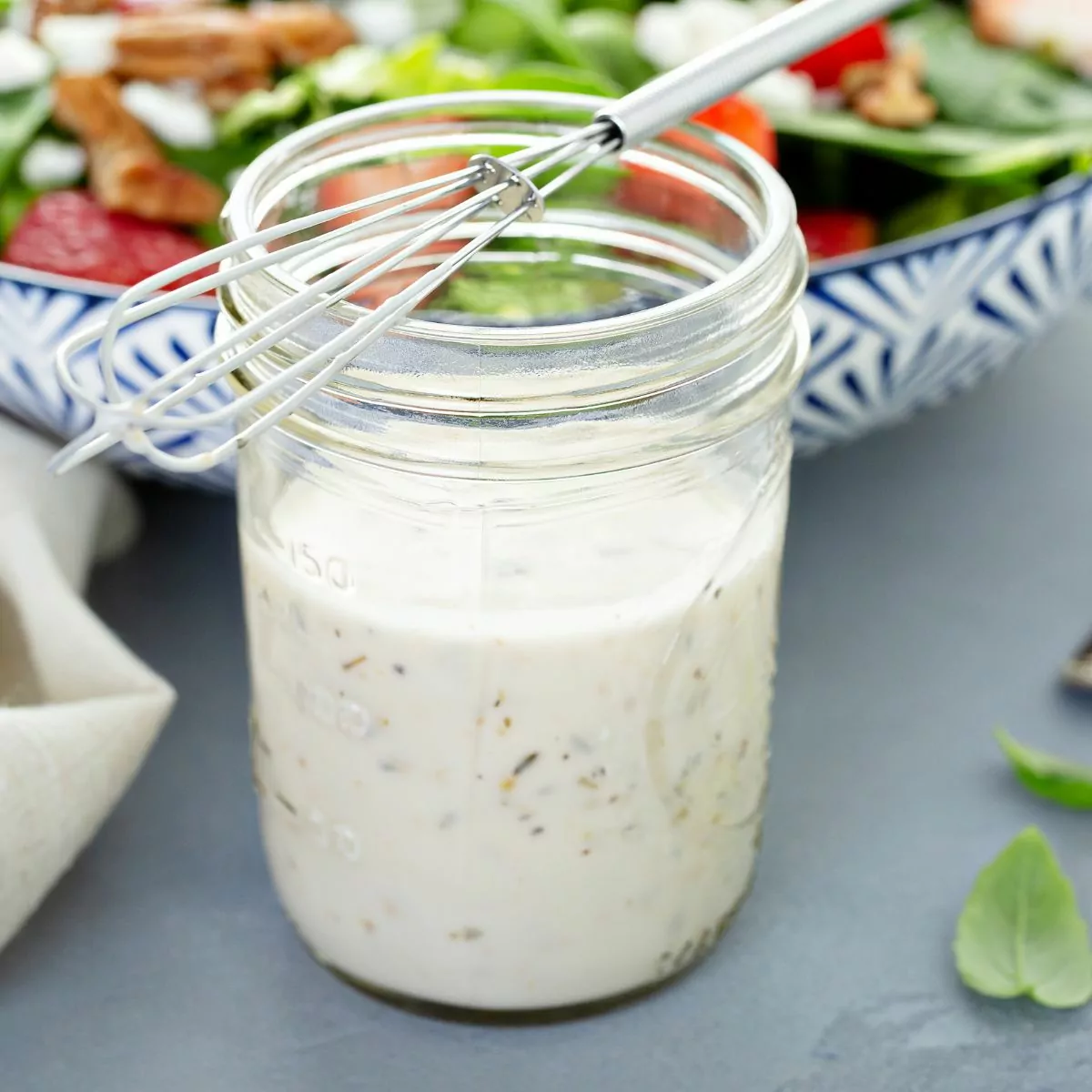 creamy salad dressing in mason jar with wire whisk on top.