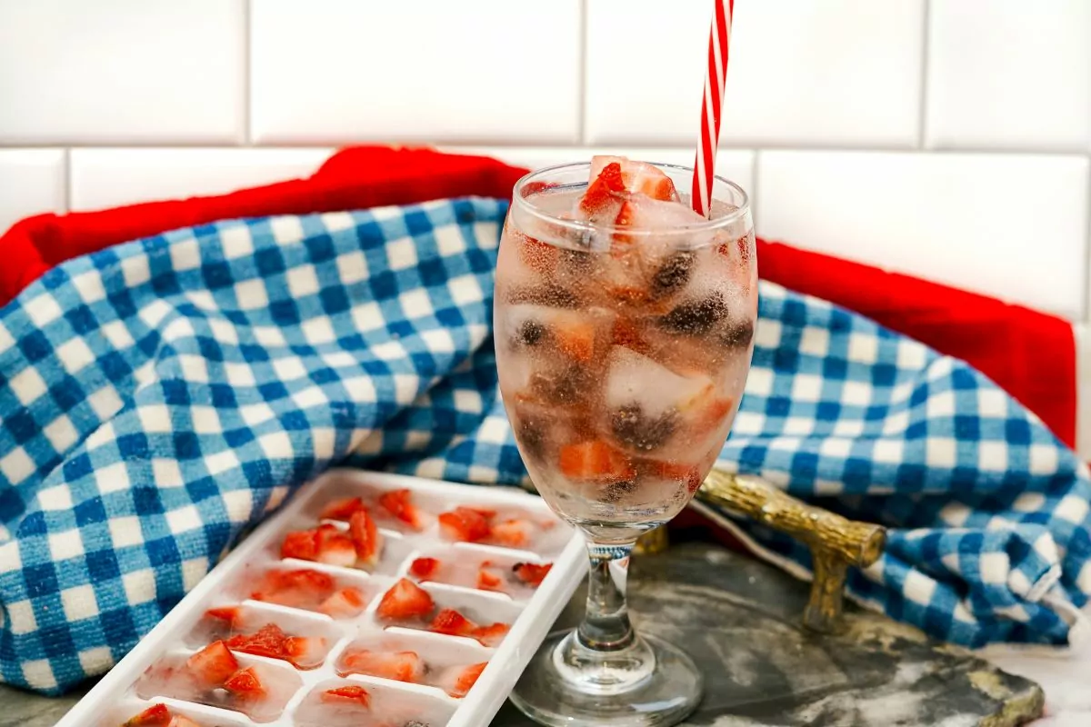 red striped straw in glass filled with water and ice cubes with frozen fruit.