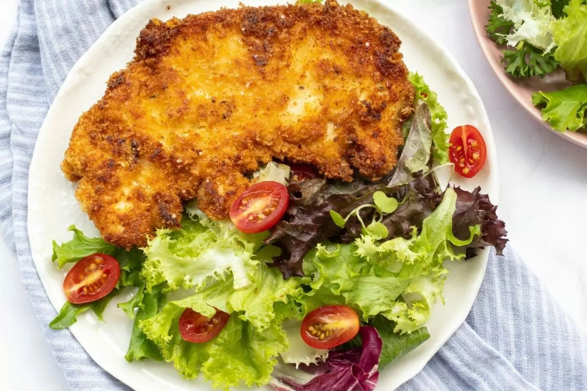 fried chicken with salad and tomatoes on white plate.