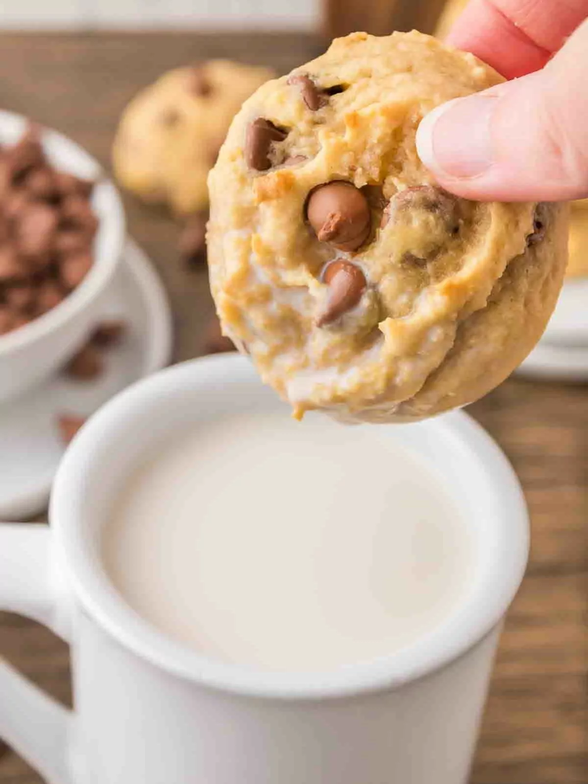 Chocolate chip cookie being dunked into a mug of milk.