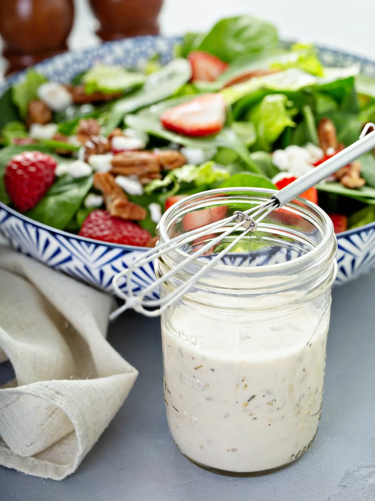 creamy salad dressing in mason jar with bowl of salad.