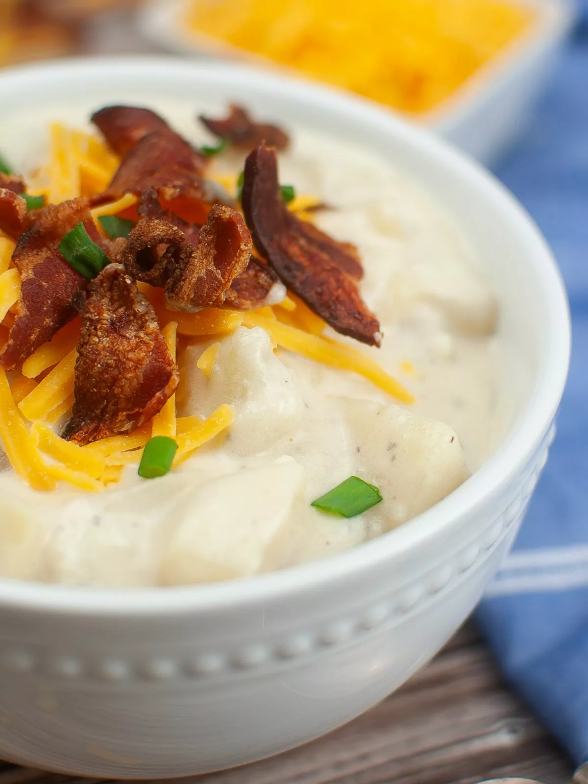 white bowl of loaded potato soup topped with cooke bacon pieces shredded cheddar and chopped chives