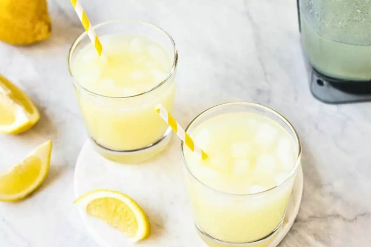 Lemonade in glasses with lemon wedges and yellow striped straws.