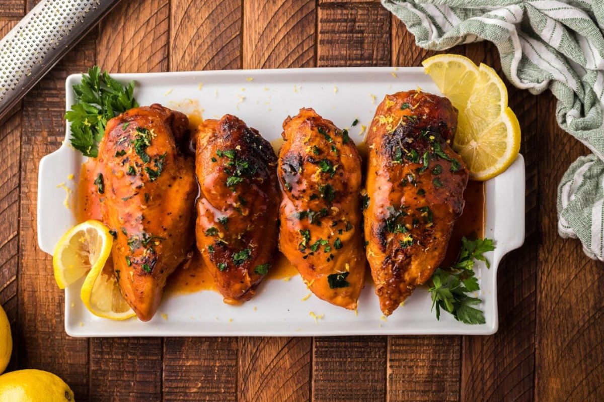 4 chicken breasts on a plate with parsley and lemon slices.