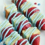 Pound cake cubes with strawberries on bamboo skewers and blue icing.