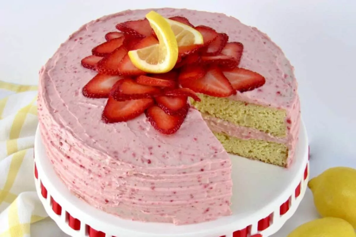 vanilla layered cake with strawberry frosting and sliced strawberries with lemon on top.