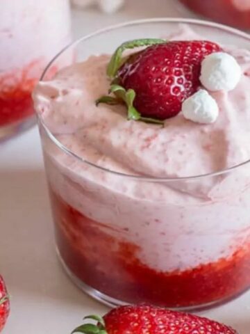 small cup of strawberry mousse with fresh strawberries scattered around.