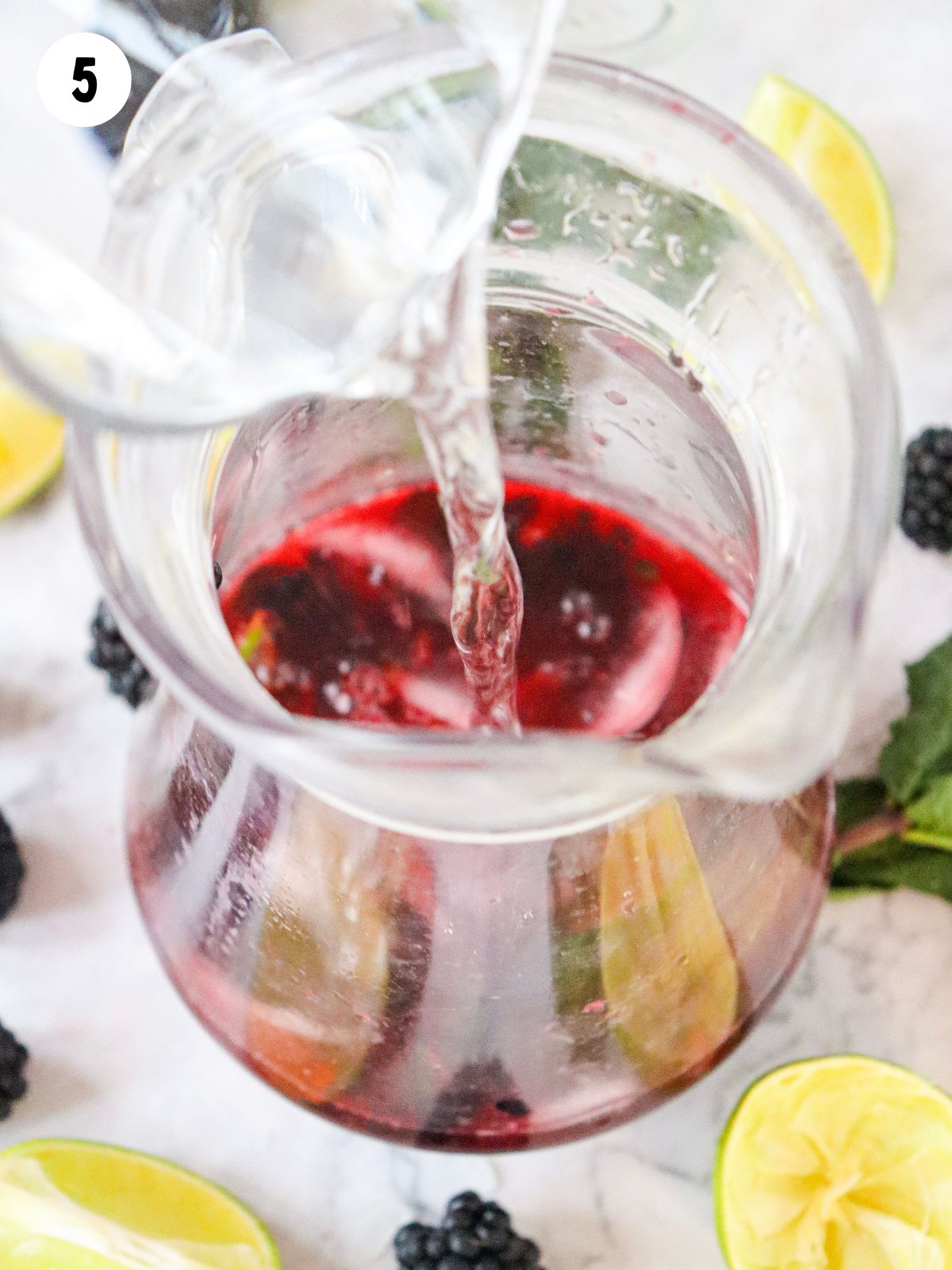 adding sparkling water to pitcher with fruit and limes.
