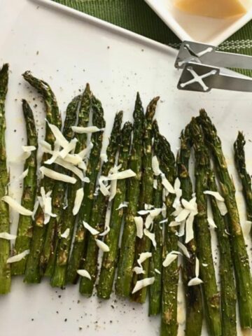asparagus roasted on white platter with Parmesan cheese.