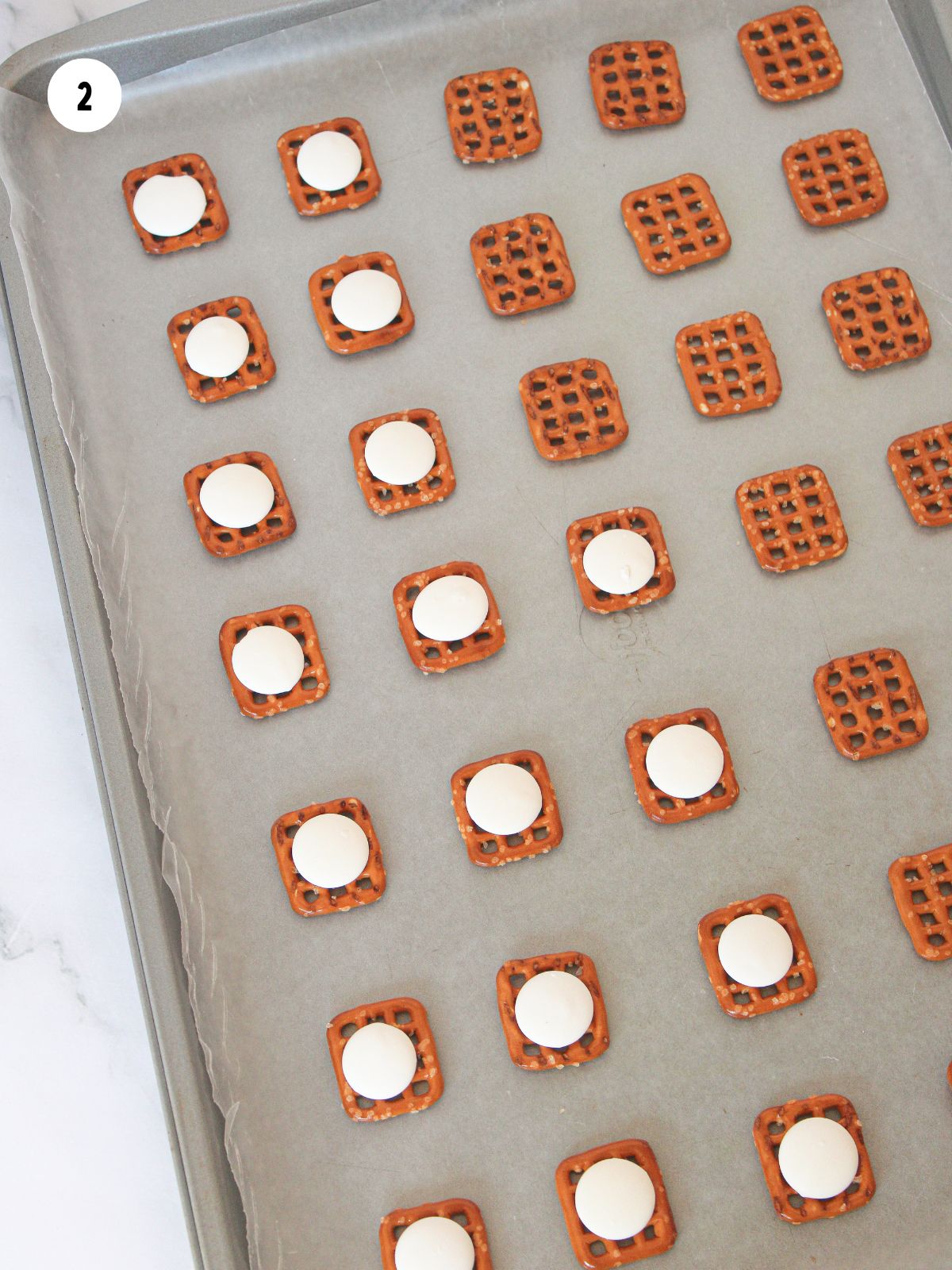 waffle pretzels with white candy melts on baking tray.