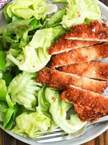 chicken on plate with salad and fork.